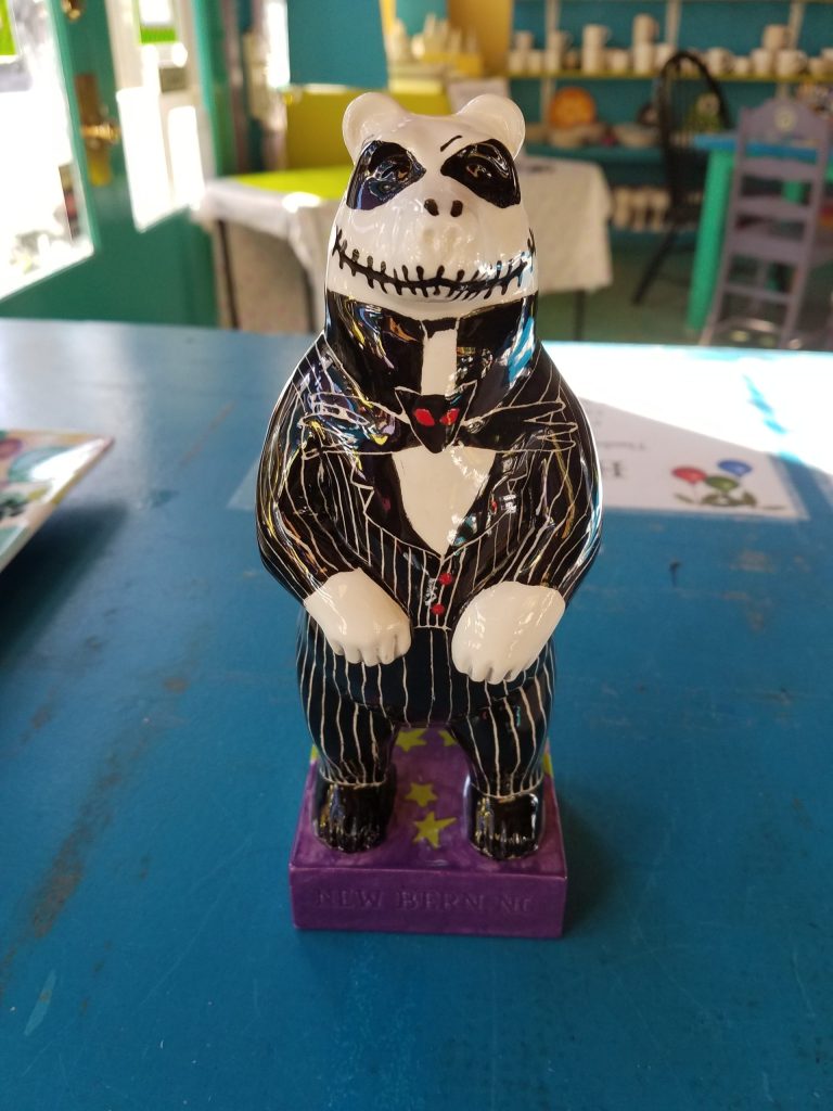 Painted figurine with a skeletal bear in a striped suit on a colorful base.