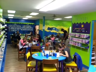Colorful craft room with people painting at tables, alphabet wall decor.
