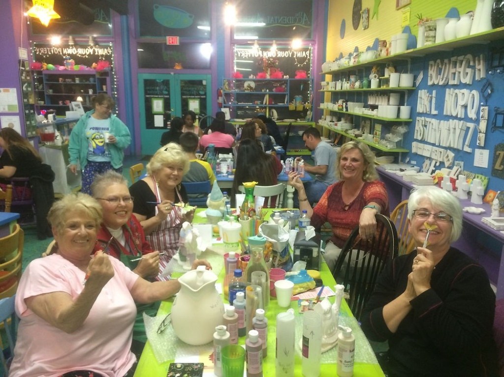 Group of women smiling and painting ceramics in a colorful studio.