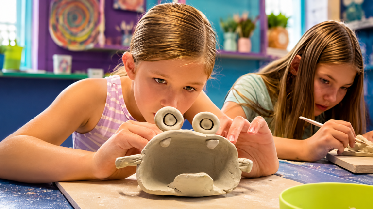 Two girls sculpting clay figures in a colorful art room.