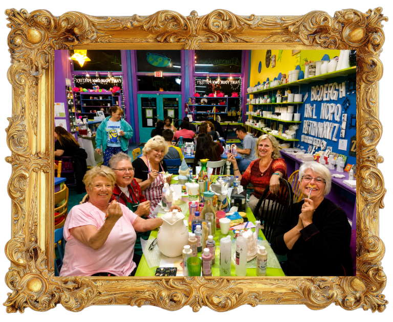Group of smiling women at a colorful table in an art studio.