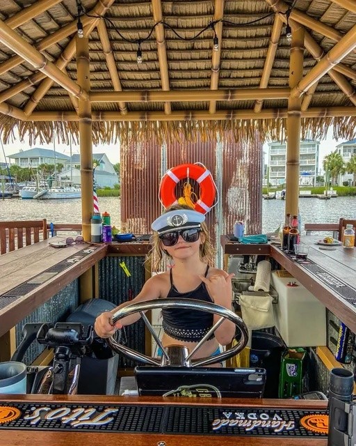 Child wearing a captain's hat steering a boat bar setup on a sunny day.