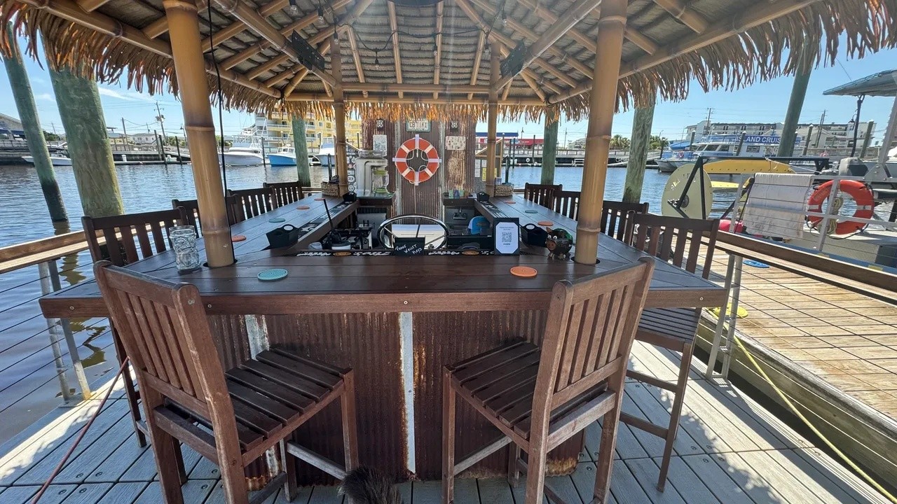 Tiki bar on a dock with stools and nautical decor overlooking a marina.