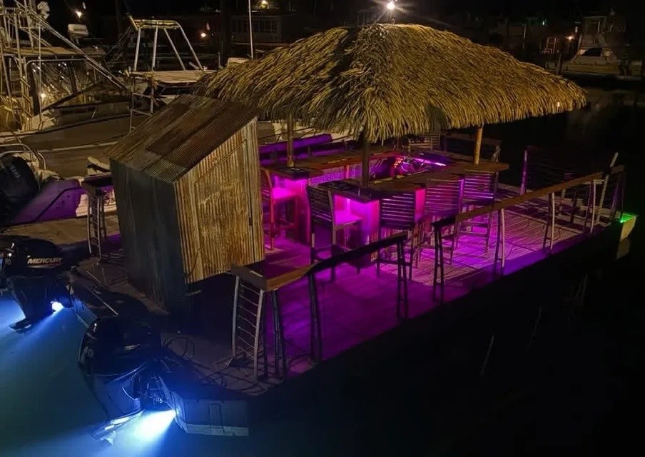 Floating tiki bar at night with purple lighting and thatched roof.