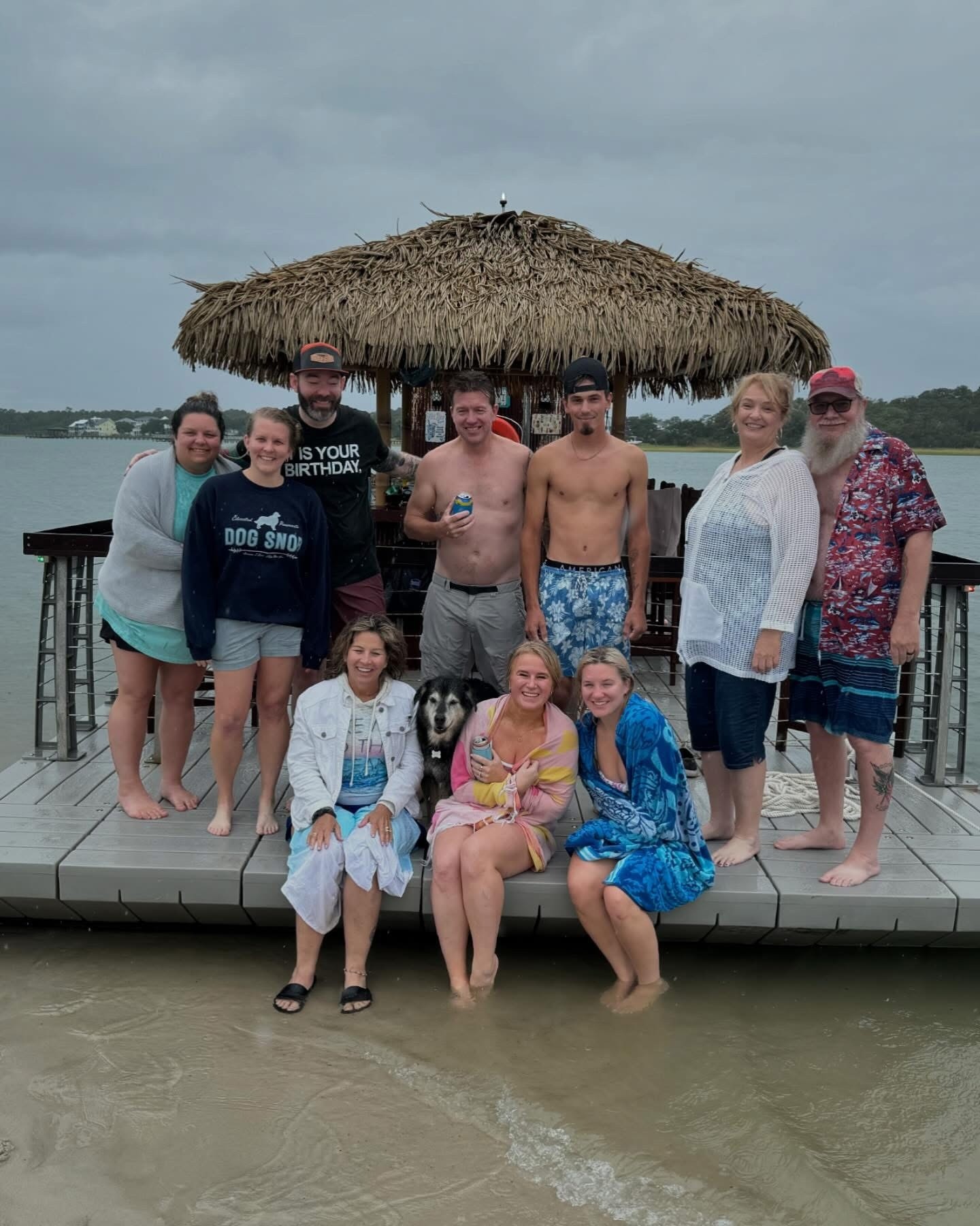 Group of people posing on a dock with a tiki hut in the background.