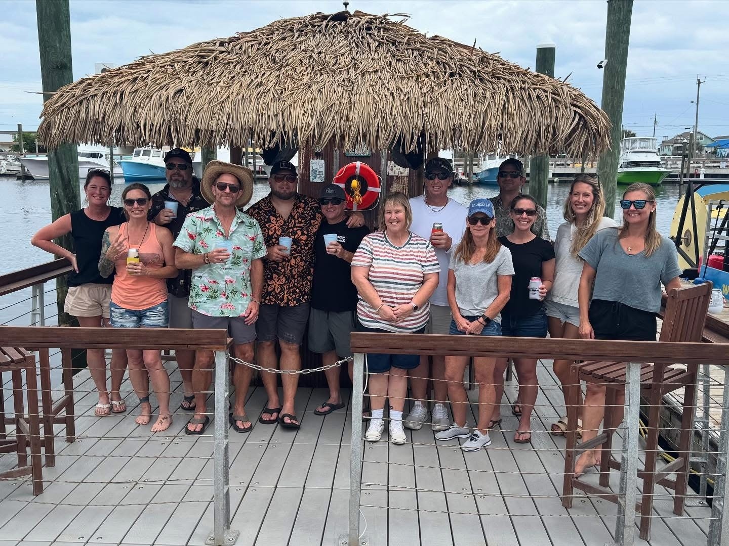 Group of people posing under a thatched roof by a marina.