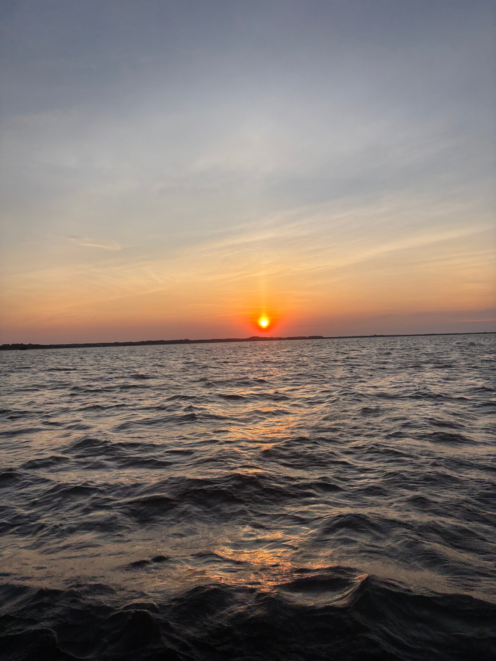Sun setting over a calm ocean with orange sky.