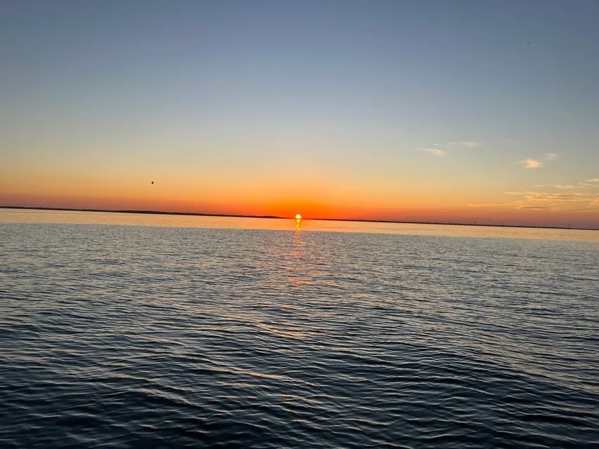 Sunset over calm ocean, clear sky with orange horizon.