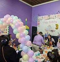 Birthday party with balloon arch and cake, people gathered around a table.