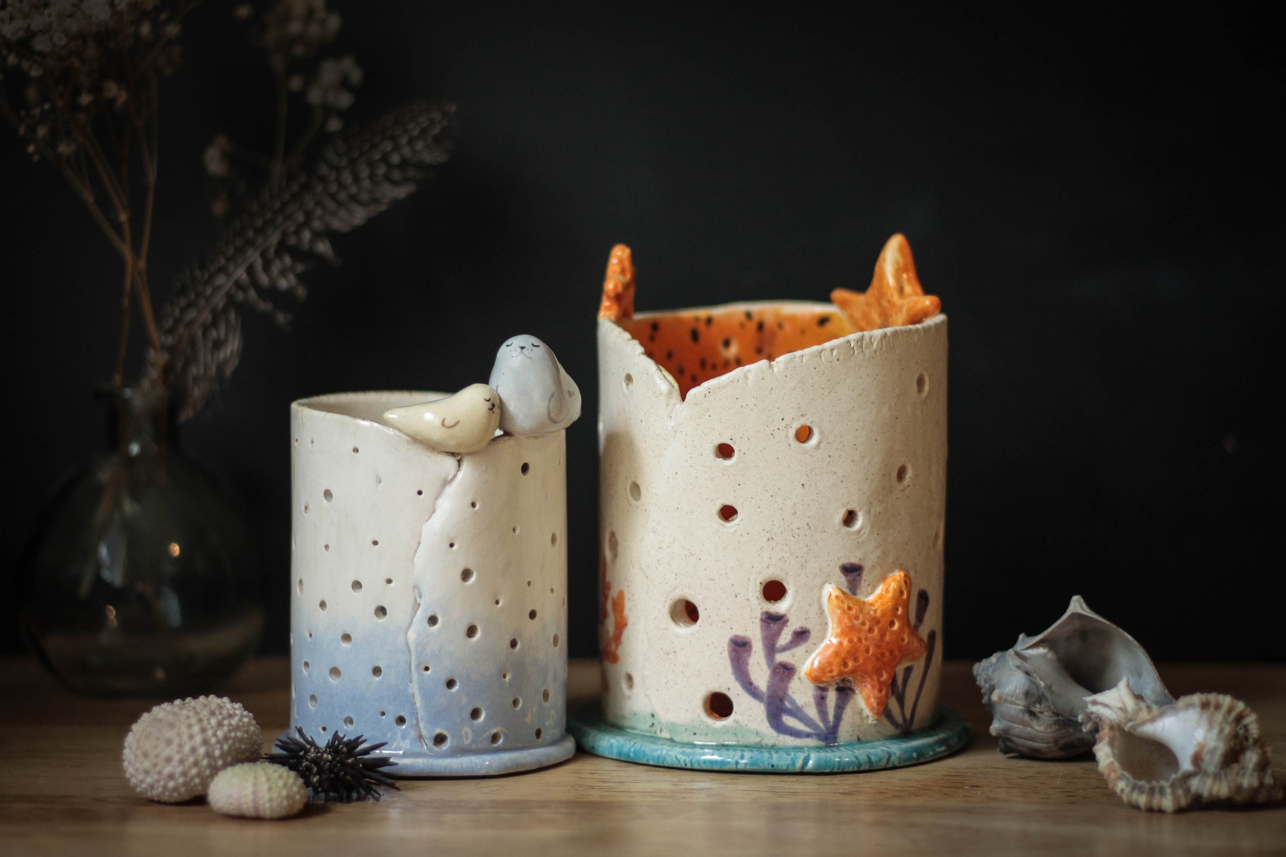 Two decorative ceramic candle holders with starfish and sea motifs on a table.