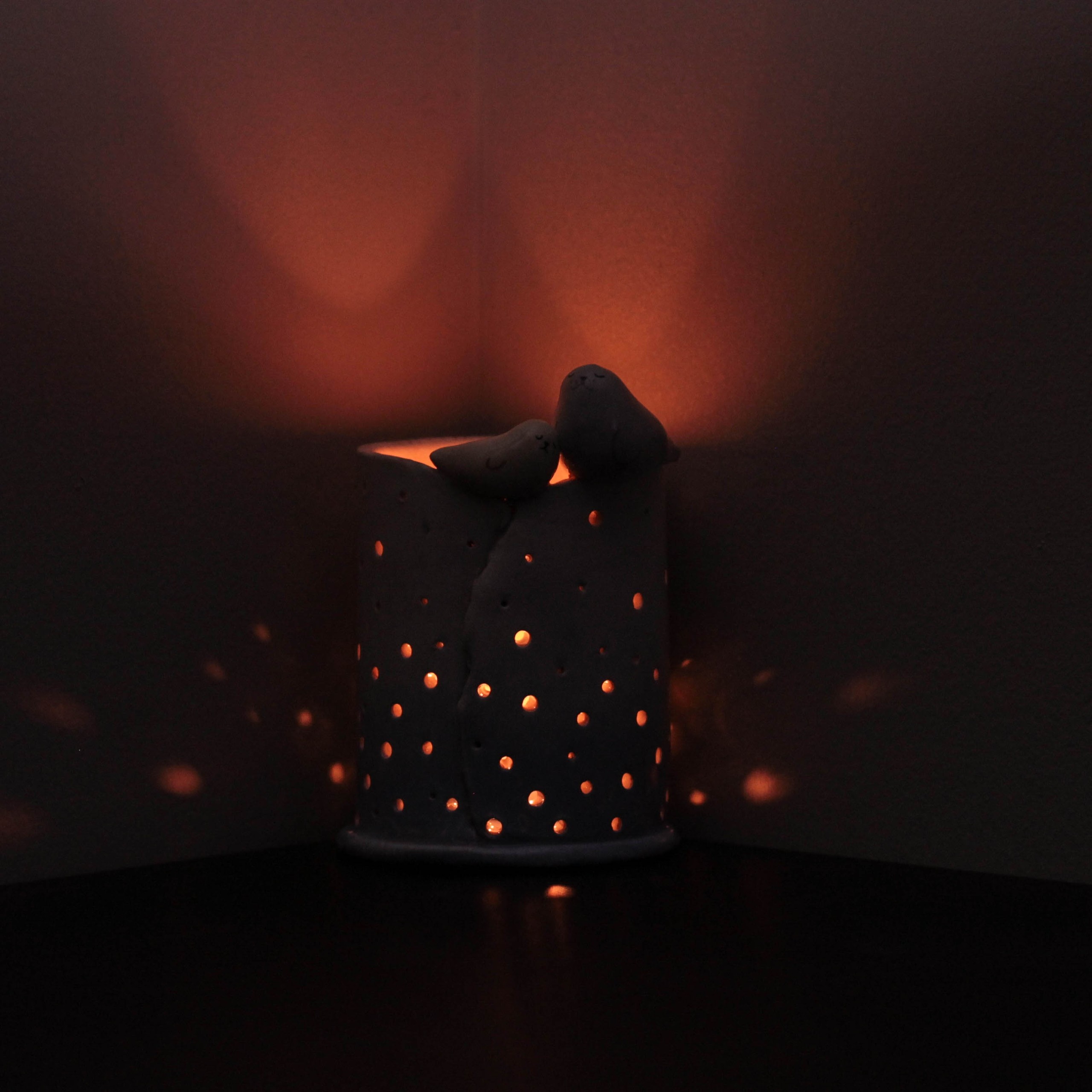 Lit candle holder with small holes casting light patterns on a dark surface.