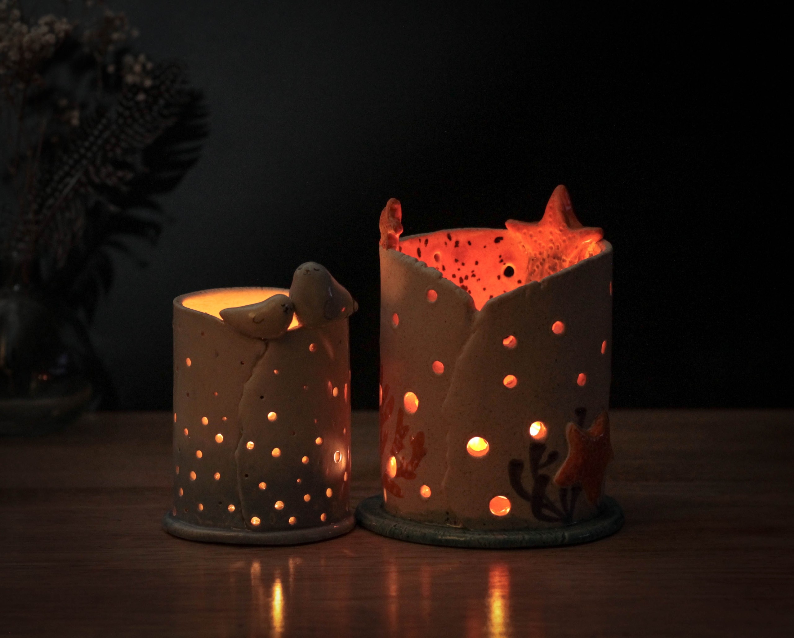Two lit ceramic candle holders with star and dot patterns on a wooden surface.