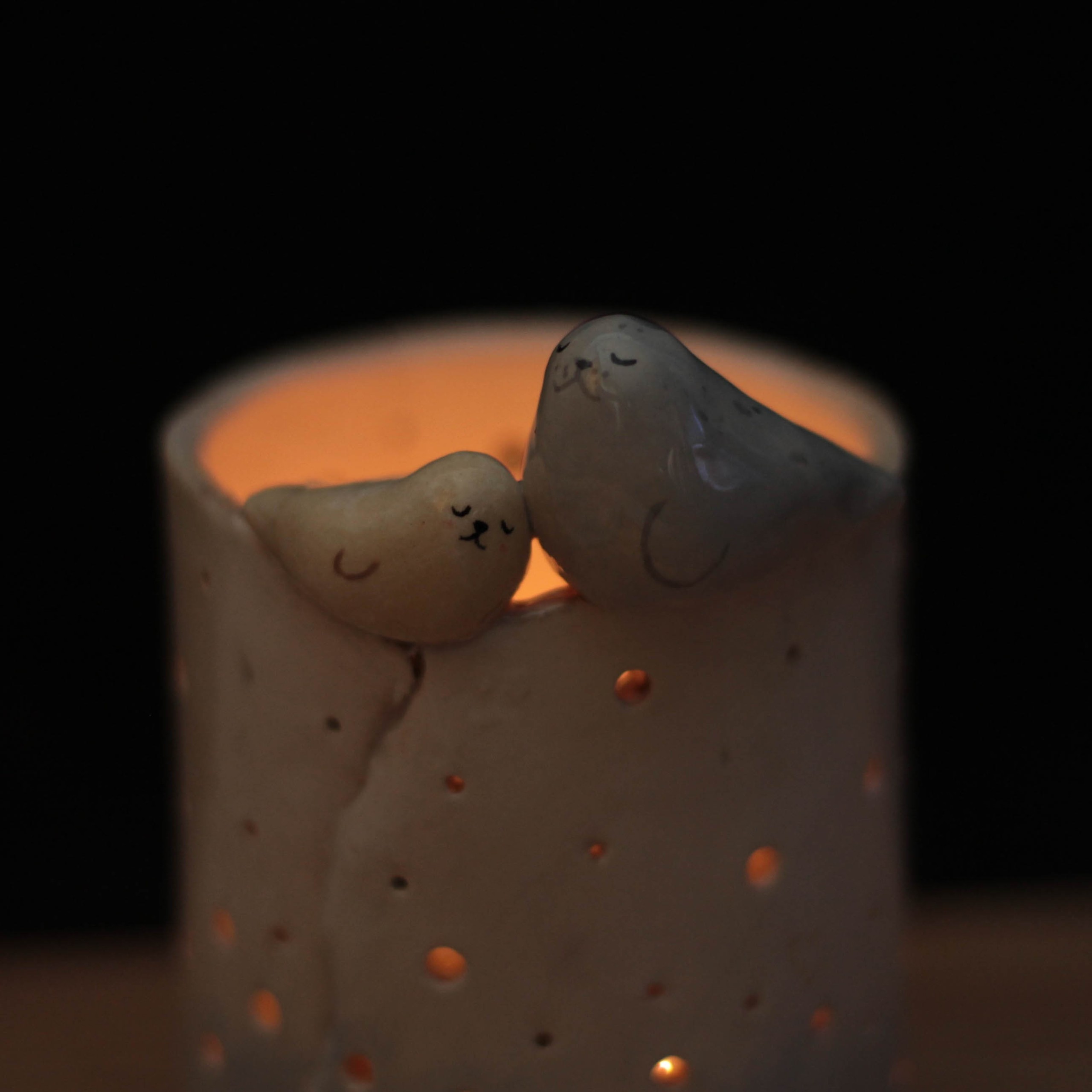 Cozy candle holder with two cute animal figures, softly lit, against a dark background.