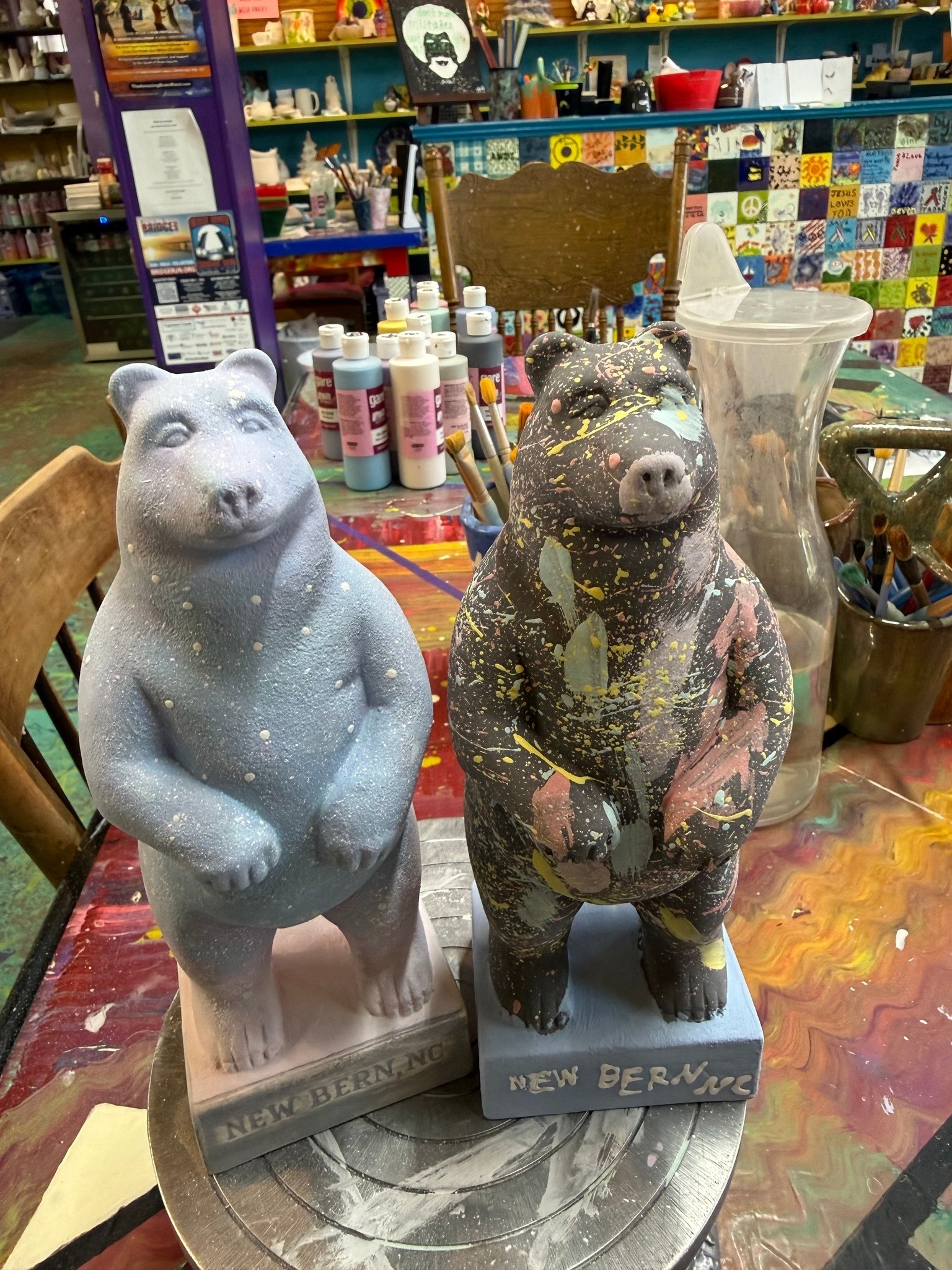 Two painted bear statues on a colorful table with art supplies.