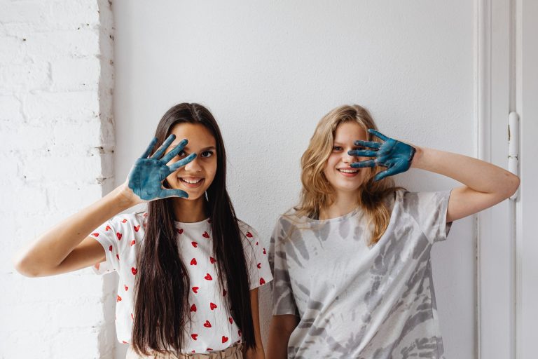 Two smiling women with painted hands covering one eye.